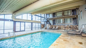 Une piscine intérieure à l’eau claire, avec un escalier en métal et un mur en pierre.