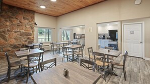 A spacious dining area with wooden tables and chairs, a stone wall, and a kitchen in the background.