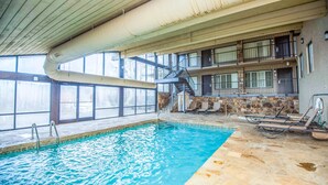 An indoor swimming pool with clear water, a metal ladder, and a stone wall.