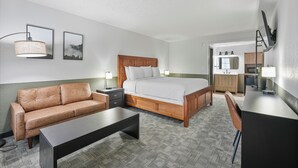 A hotel room with a bed, a sofa, a desk, a chair, a lamp, and a mirror.