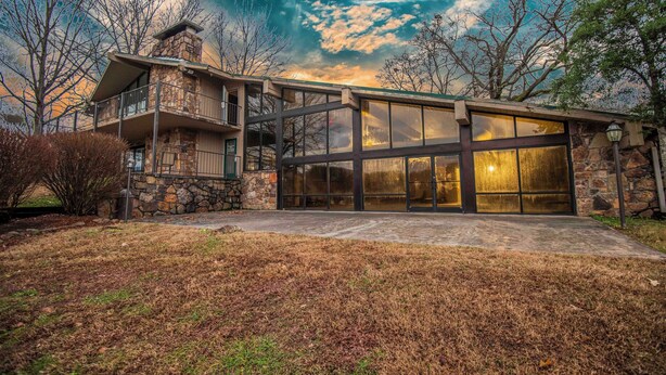 A modern two-story house with a stone facade, large glass windows, and a balcony.