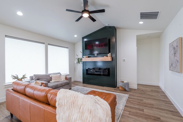 A modern living room with a leather sofa, a fireplace, and a large TV screen displaying "NETFLIX".