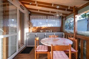 A wooden deck with a round table and chairs, a small kitchen area, and a view of the outside.