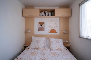 Une chambre à coucher comprenant un lit, deux tables de chevet, une étagère murale avec des livres et une fenêtre.