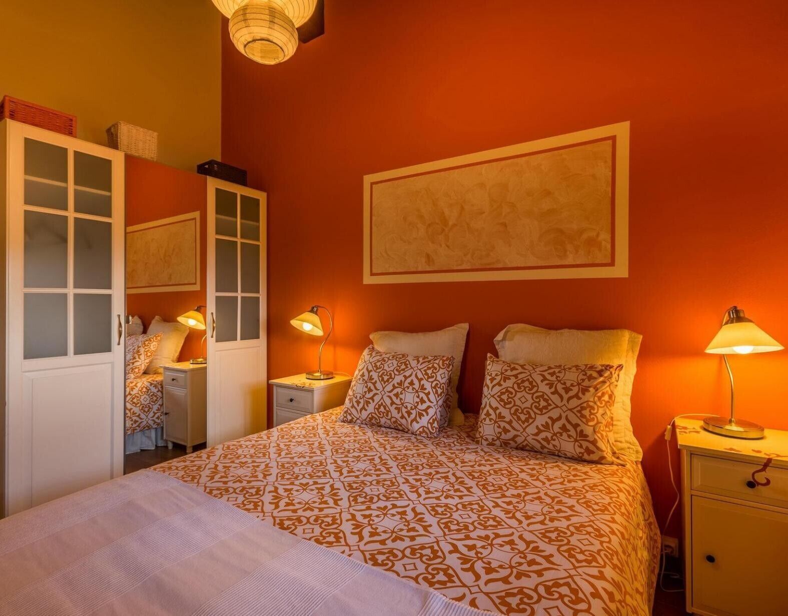A bedroom with a bed, two bedside tables, a wardrobe, and a wall-mounted artwork.