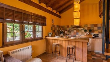Cozinha com vigas de madeira, painel de azulejos xadrez, área de bar com banquetas e janela com persianas.