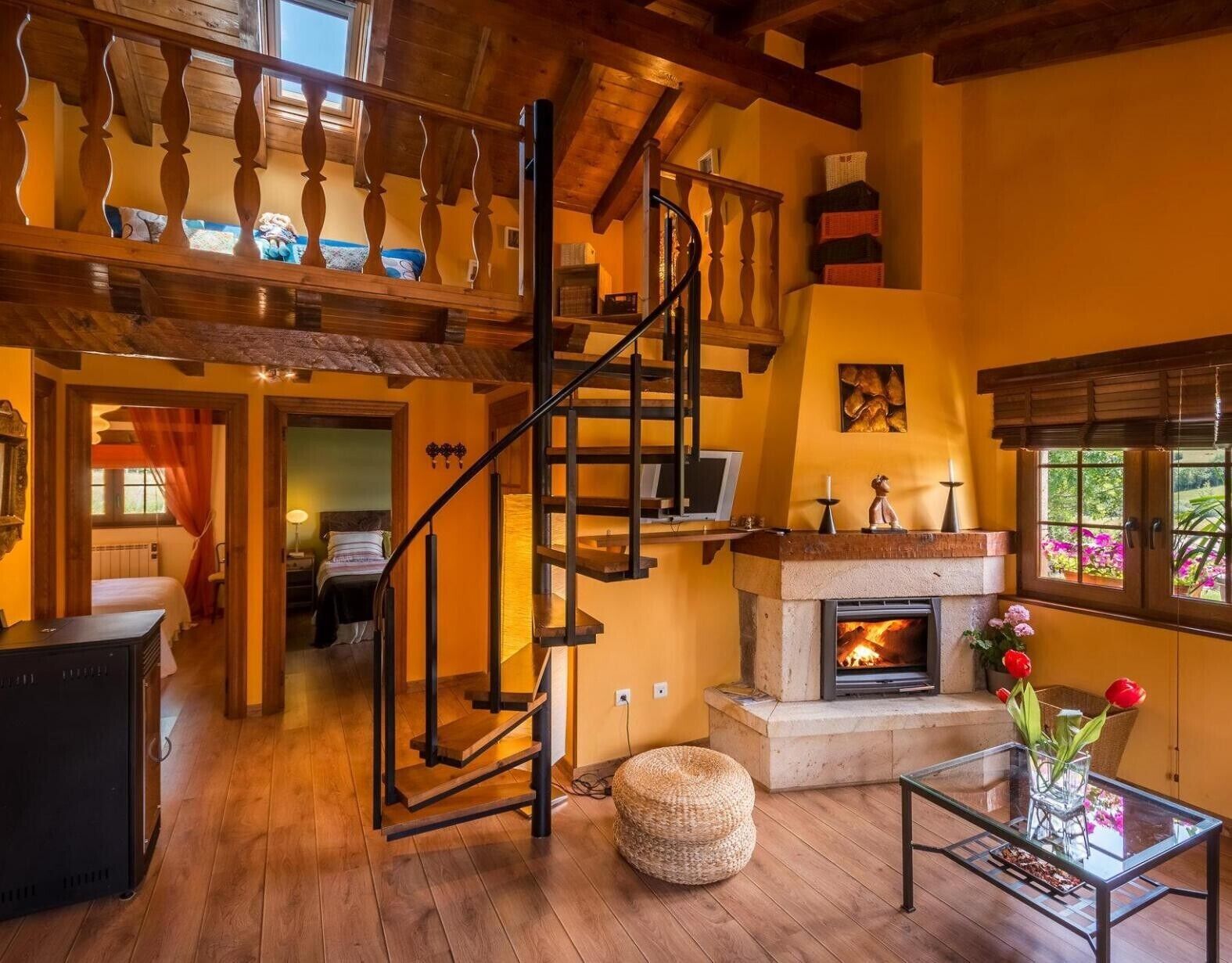 Amplia sala de estar con escalera de madera, chimenea y mesa de centro de vidrio.