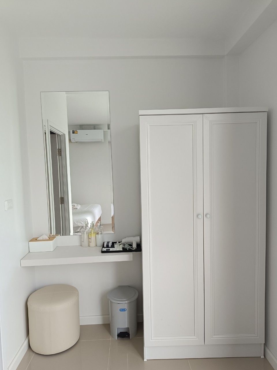 Un baño minimalista con un espejo grande, un tocador blanco, un inodoro y un armario.