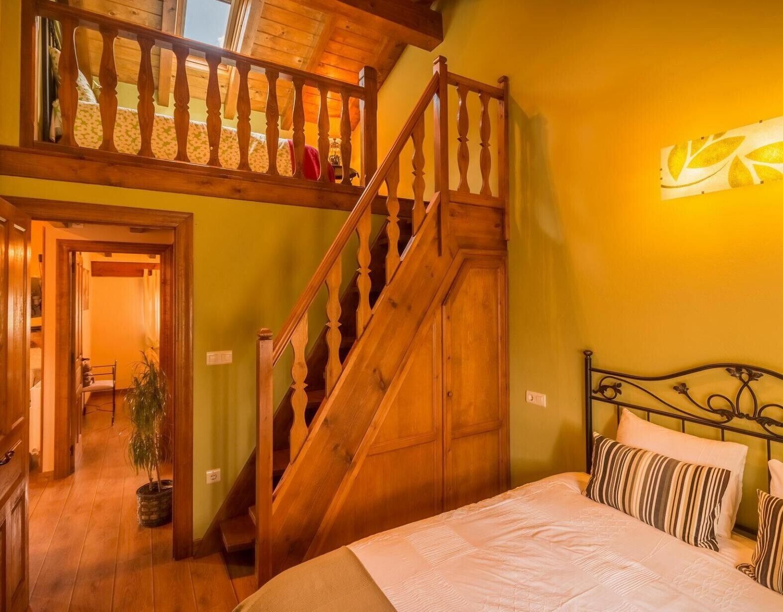 Une chambre avec un escalier en bois, un lit agrémenté d’oreillers à rayures et un luminaire fixé au mur.