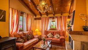 Un salon chaleureux avec des poutres en bois, une cheminée, des rideaux à rayures et un lustre.