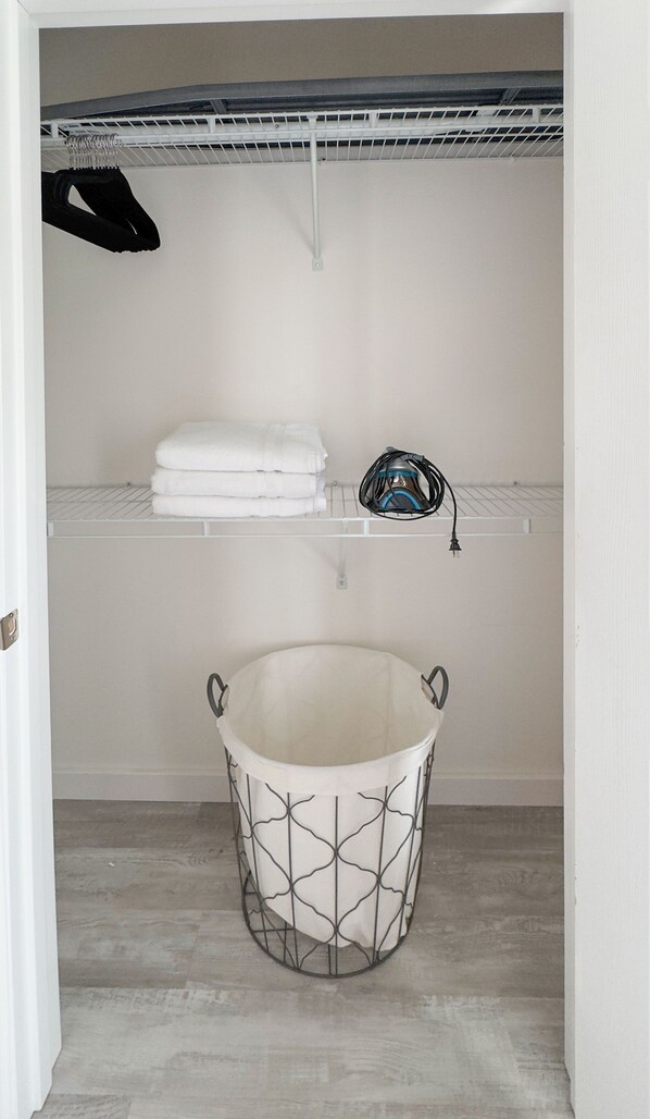 A laundry room with a metal laundry basket, a shelf with folded towels, and a ceiling fan.