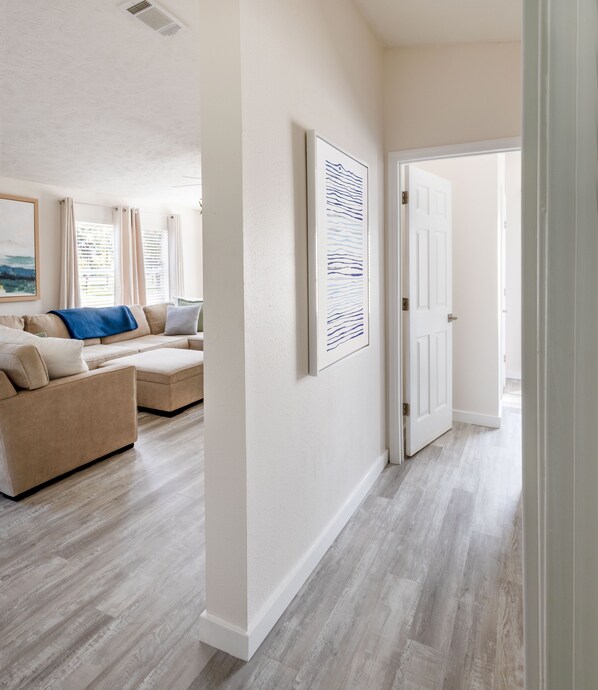 A hallway with a beige sofa set, a framed artwork on the wall, and a door leading to another room.