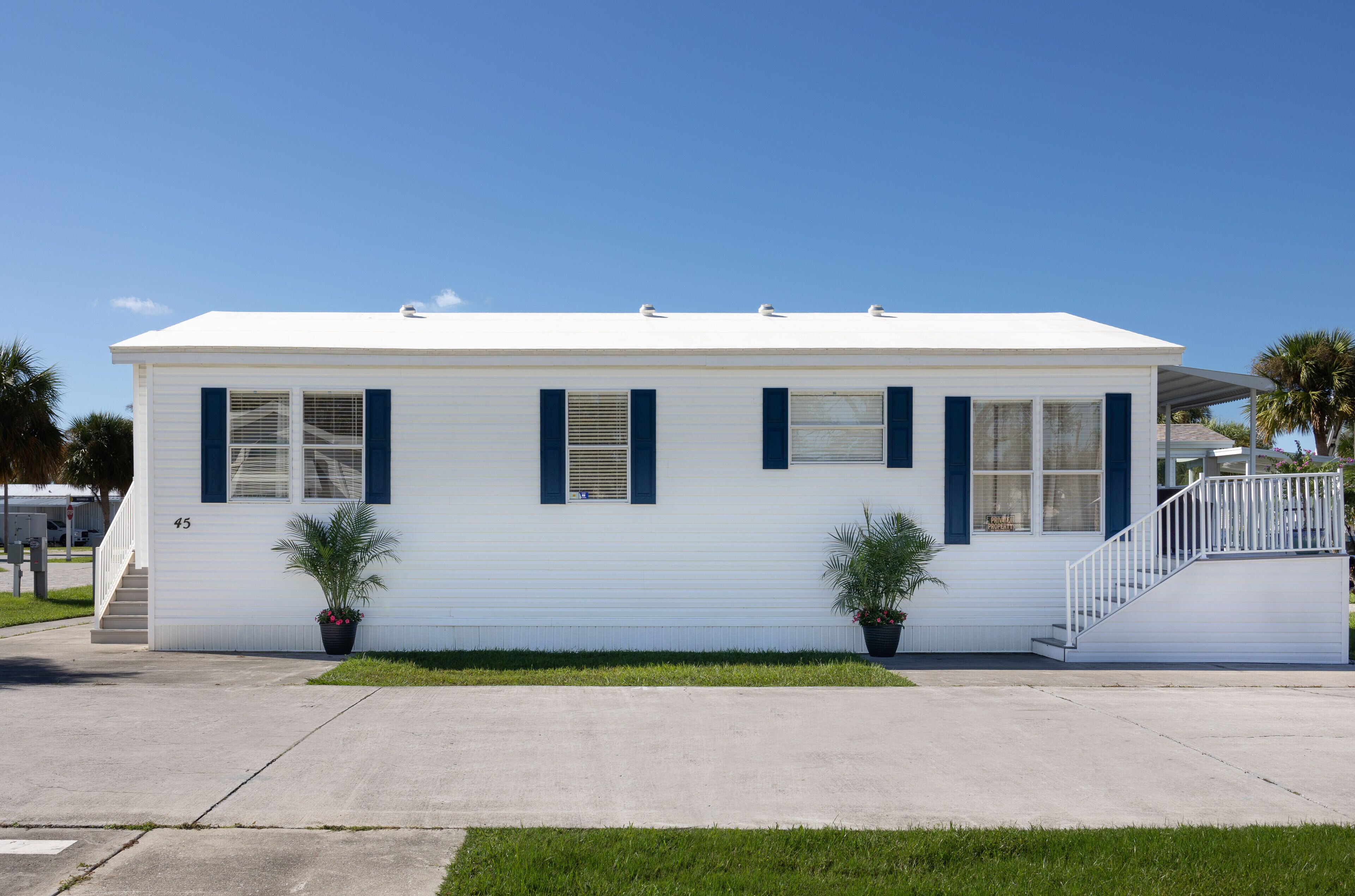 A single-story white building with blue shutters, a covered porch, and two potted plants.
