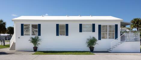 A single-story white building with blue shutters, a covered porch, and two potted plants.