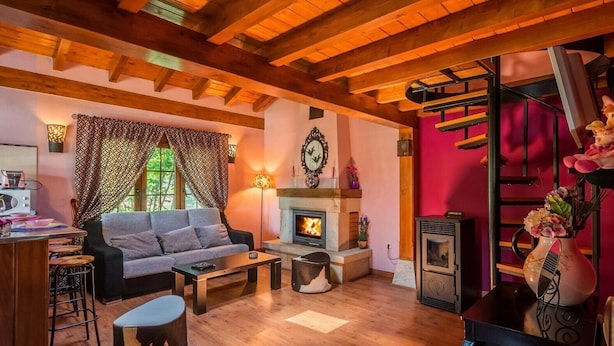 A cozy living room with a fireplace, wooden beams, a sofa, and a dining area.
