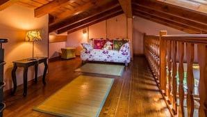 A cozy attic room with a wooden ceiling, a sofa with floral cushions, a small table, and a bench.
