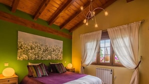 A bedroom with a bed, a radiator, a window with curtains, a wall painting, and a wooden ceiling.
