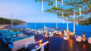 A deck with outdoor seating, a view of the sea, and a tree overhead.