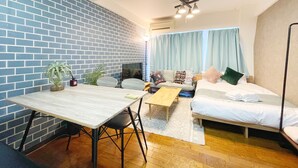 A compact room with a brick wall, a bed, a sofa, a dining table, and a small kitchen area. - LVB Shibuyadogenzaka (Tokyo)