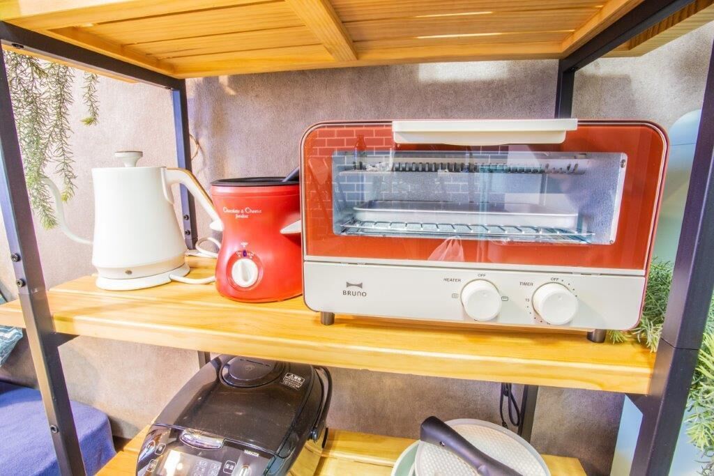 Une petite cuisine équipée d’un four grille-pain rouge, d’une bouilloire blanche et d’une machine à café, le tout posé sur une étagère en bois.
