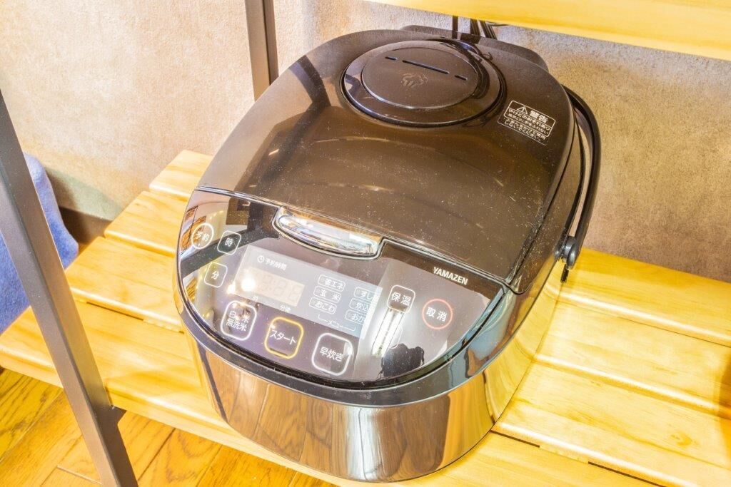 A compact, modern electric rice cooker with a digital interface, placed on a wooden surface.