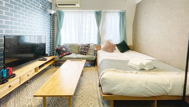 A modern hotel room with a brick wall, a flat-screen TV, a wooden bench, a bed with white bedding, and a ceiling light fixture. - LVB Shibuyadogenzaka (Tokyo)