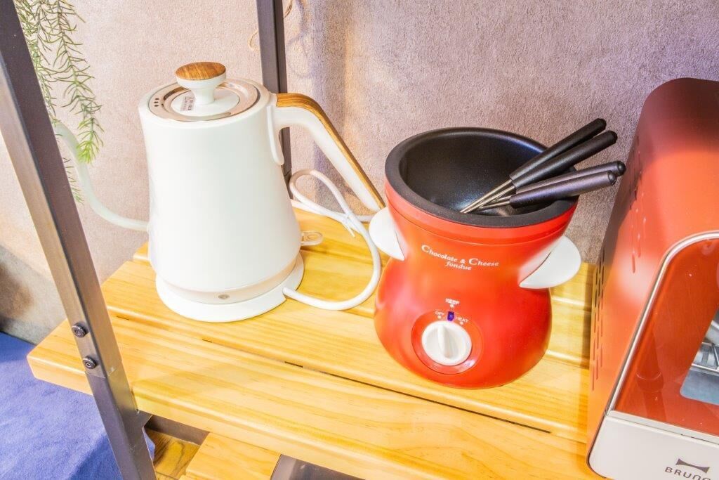 Una cocina con un hervidor eléctrico blanco, una olla para fondue roja y una estufa eléctrica roja.