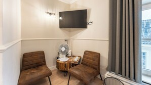 Una habitación de esquina con dos sillones de cuero marrón, una mesita de madera con un abanico y un televisor montado.