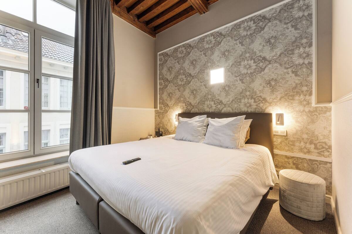 Een hotelkamer met een groot bed, een raam met gordijnen, een wandlamp en een radiator.