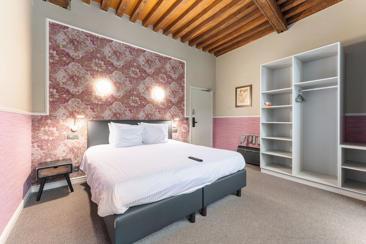 Een slaapkamer met een bed, nachtkastje, kledingkast en een wand met bloemenprint.