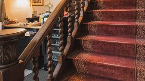 Una imponente escalera con barandales de madera decorados y peldaños alfombrados de rojo.