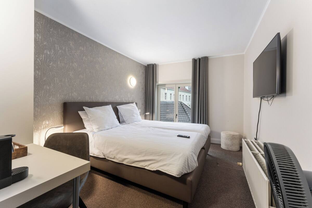 Hotelkamer met een bed, bureau, stoel, televisie, raam met gordijnen en een radiator.