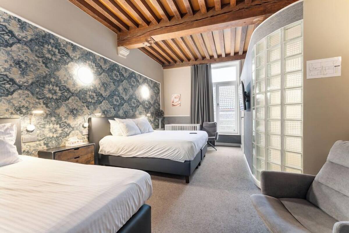 Een moderne slaapkamer met twee bedden, een houten plafond en een groot raam met zonwering.