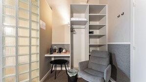 Un espacio habitable compacto con kitchenette, un sillón gris, una mesita y un estante blanco.