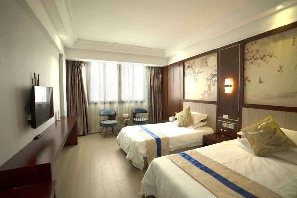 A hotel room with two beds, a TV, a desk, and a chair.