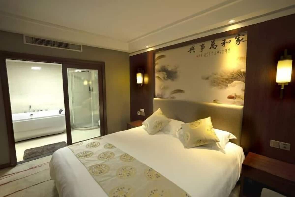 A hotel room with a large bed, a bathroom with a bathtub, and a sliding glass door leading to a balcony.