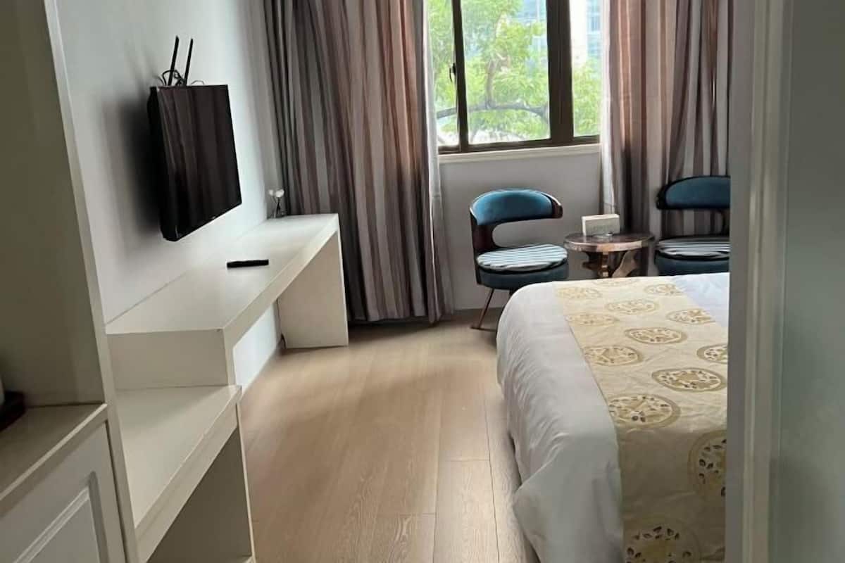 A hotel room with a bed, a desk, a chair, a small table, and a TV mounted on the wall.