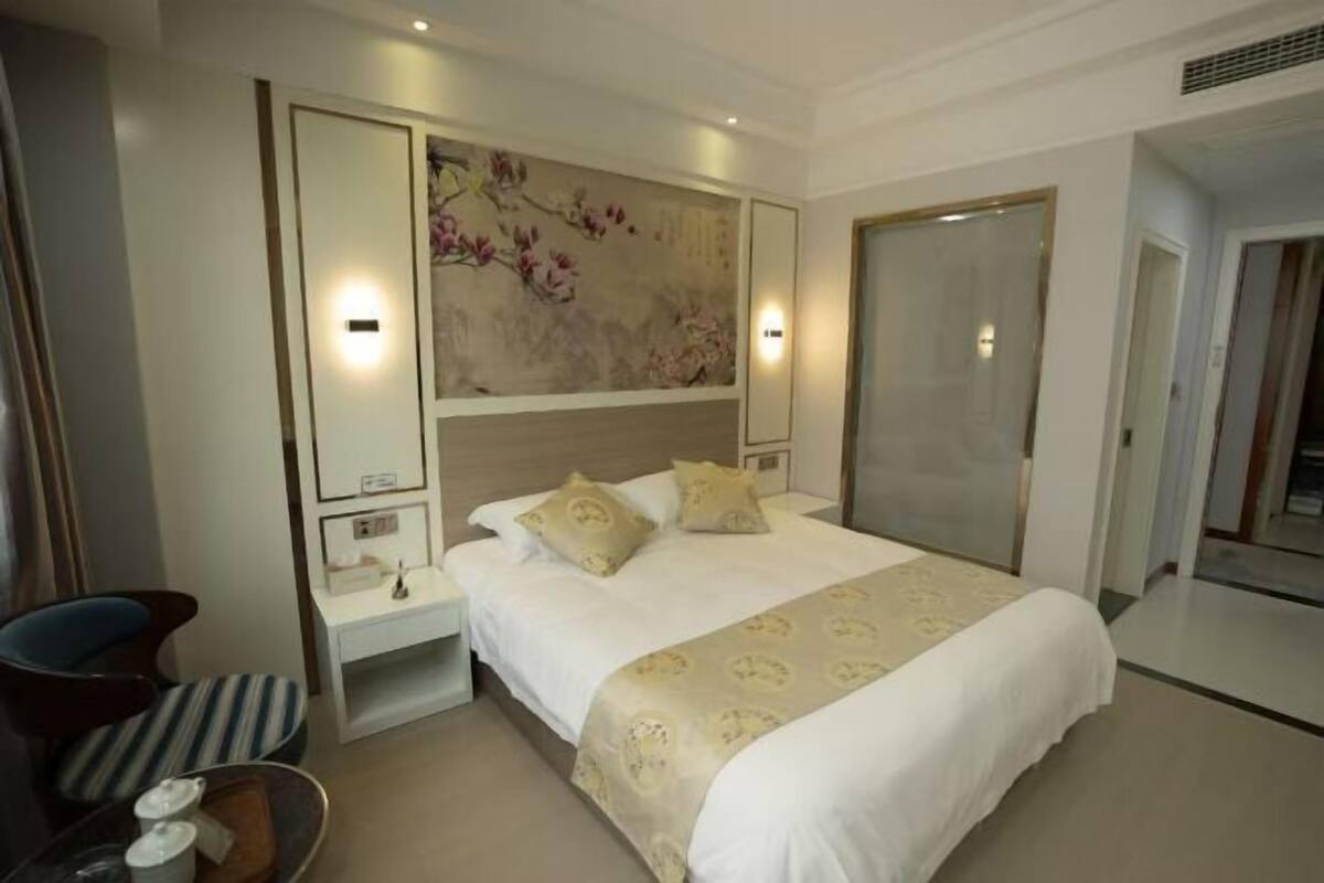 A hotel room with a large bed, bedside tables, a chair, a desk, and a wall-mounted artwork.
