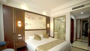 A hotel room with a bed, a bedside table, a chair, a wall with a decorative painting, and a bathroom door. - Youth Holiday Hotel (Fuding)