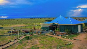 Un paisaje rural con un edificio grande de techo azul, rodeado de campos abiertos y un cielo despejado.
