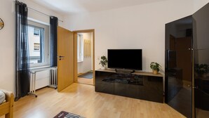 A modern living room with a flat-screen TV, wooden flooring, a black cabinet, and a window with curtains. - Apartment 'Tifra-living' with Wi-Fi (Velbert-Neviges)