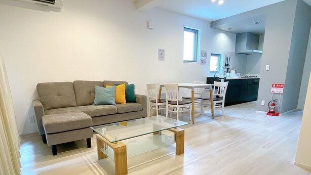 A modern living room with a glass coffee table, a sofa with cushions, and a dining area with chairs. - Palace Oceanside (Chatan)