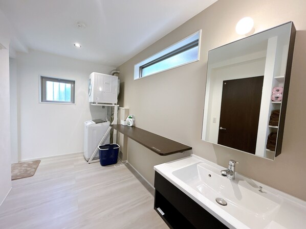 A modern bathroom with a large mirror, a white sink, and a built-in washing machine. - Palace Oceanside (Chatan)