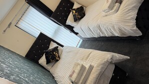 Une chambre d’hôtel avec deux lits, une grande fenêtre avec des stores, un lustre et une moquette de couleur sombre.
