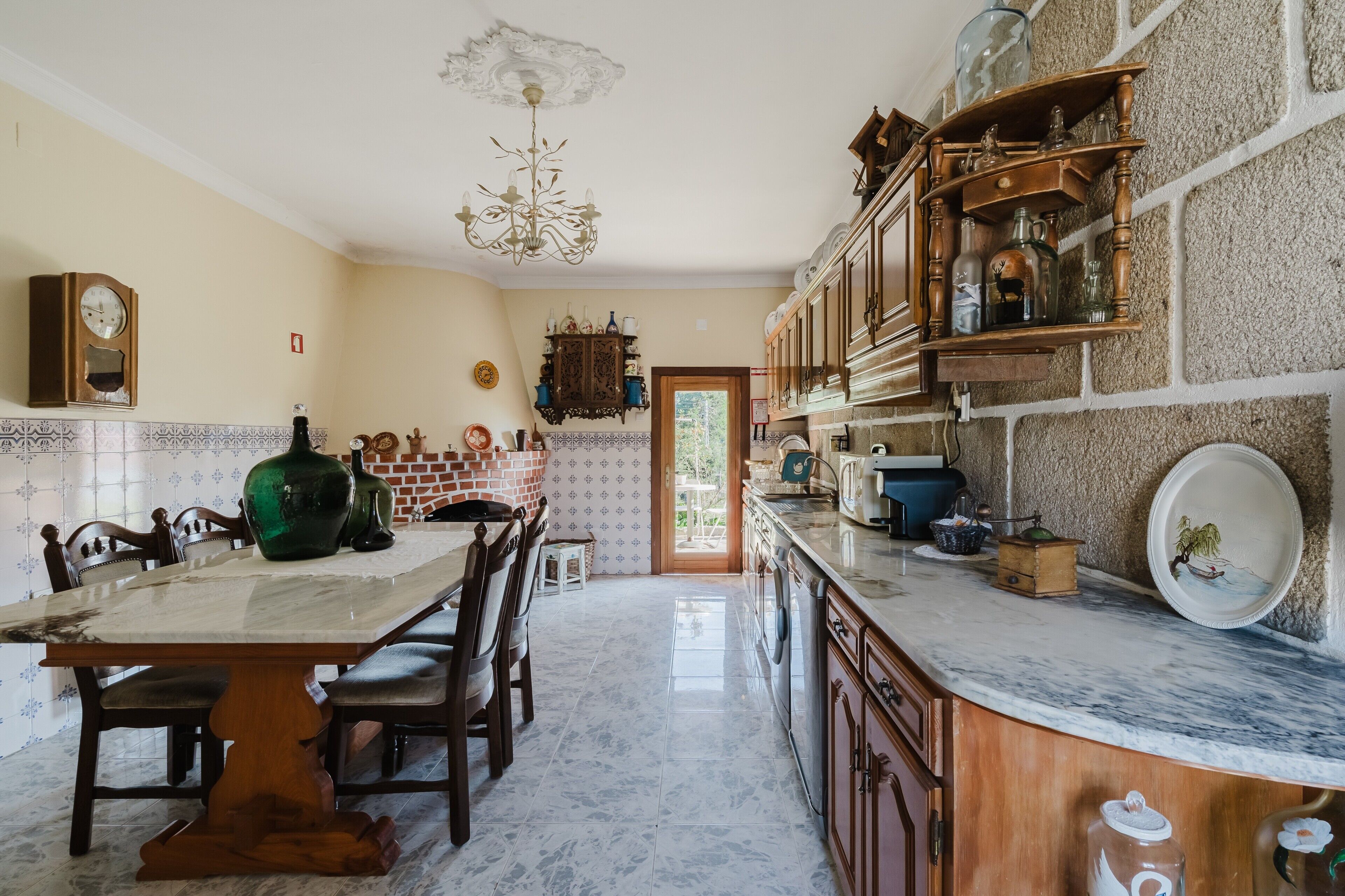 A kitchen with a marble countertop, wooden cabinets, a chandelier, and a dining area with chairs and a table.