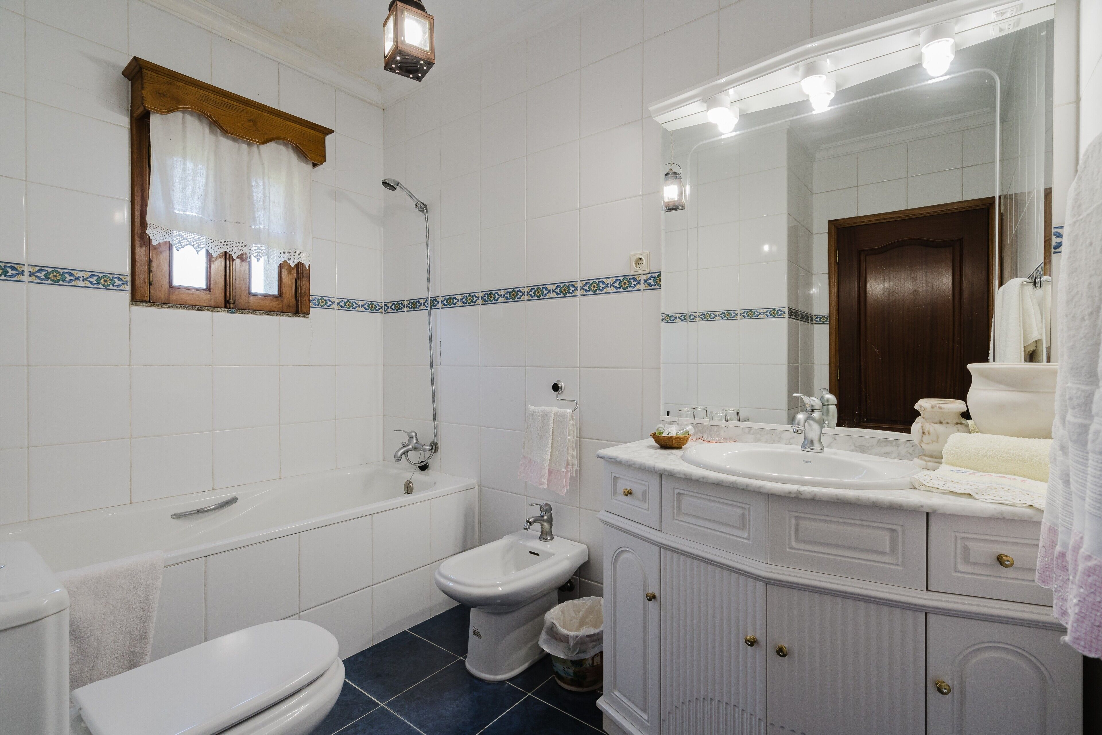 A bathroom with a bathtub, bidet, toilet, vanity with mirror, and tiled walls.