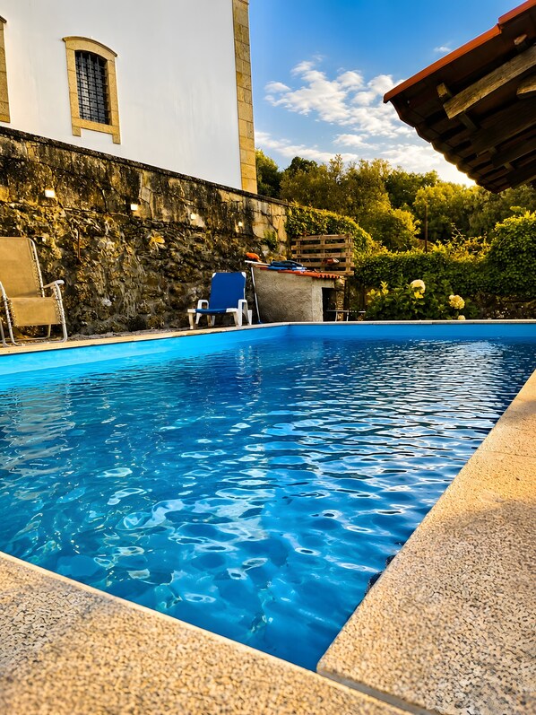 Une piscine à l’eau d’un bleu cristallin, entourée d’un mur de pierre et d’une terrasse en bois.