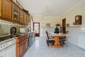 A kitchen with wooden cabinets, a sink, a stove, a microwave, and a dining area with a table and chairs. - Country House 'Quinta Do Passal - Gondoriz' with Mountain View, Wi-Fi and Air Conditioning (Arcos de Valdevez)