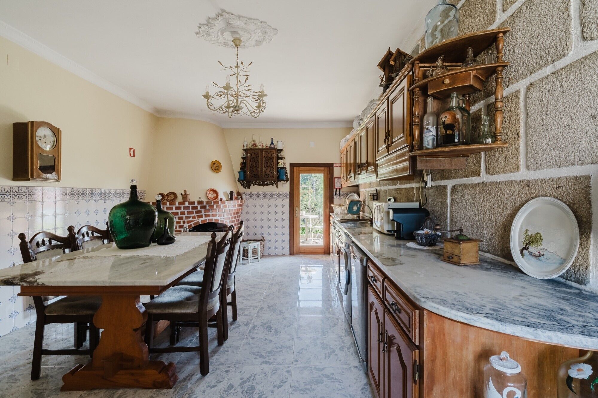 A kitchen with a marble countertop, wooden cabinets, a chandelier, and a brick fireplace.