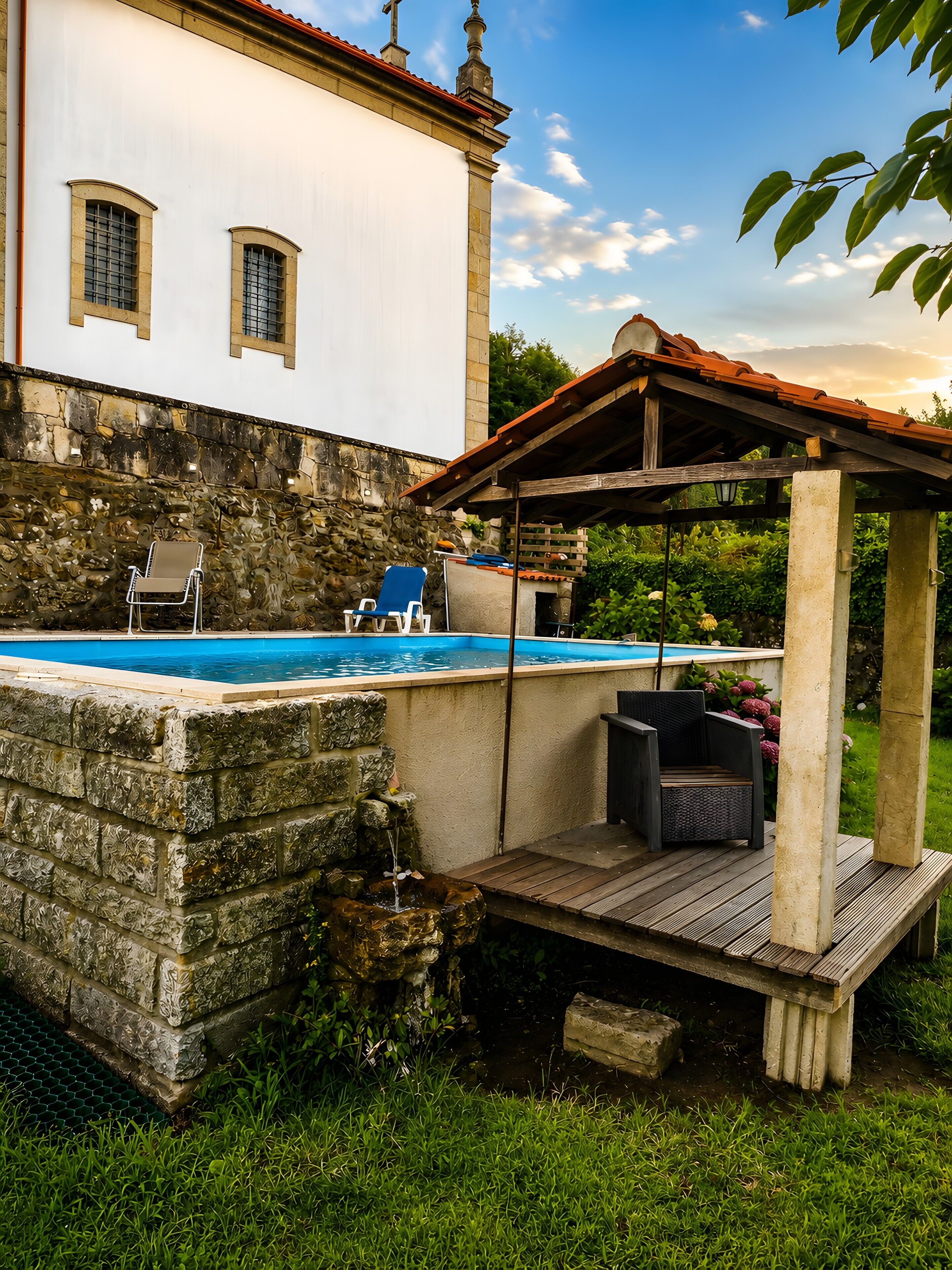 A swimming pool with a stone wall, a wooden deck, and a gazebo.